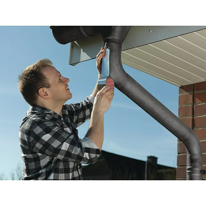 Tesa AluminiumbandSilber, 10 m x 50 mm - Ein Mann repariert ein Fallrohr mit starkem Klebeband, um Schäden zu beheben. Praktische Lösung für schnelle Reparaturen im Außenbereich.