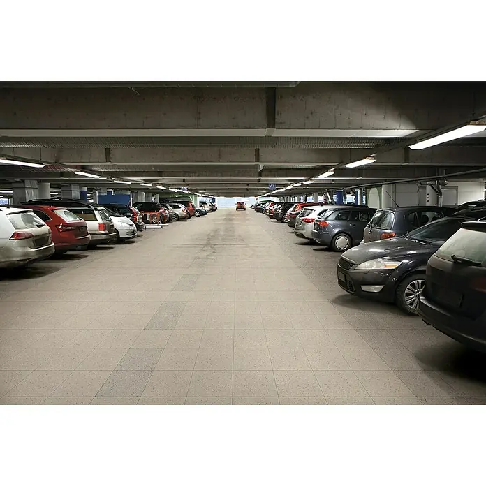 Feinsteinzeugfliese Pompei - 30 x 30 cm, Sand, Matt - Eine lange Reihe geparkter Autos in einem Parkhaus unter hellen Leuchtstoffröhren und Betonstützen.