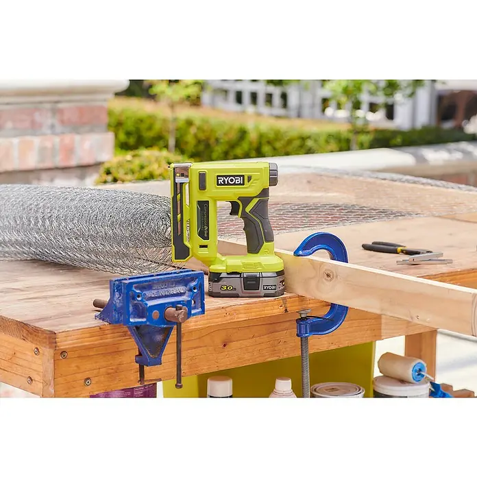 Ryobi ONE+ Akku-Tacker R18ST50-0 - 18 V, Li-Ionen, Anzahl Akkus: Ohne Akku - Der Ryobi-Tacker, ein gelbes Elektrowerkzeug mit Akku, steht auf einer Werkbank neben einem Drahtgeflecht und Werkzeugen.