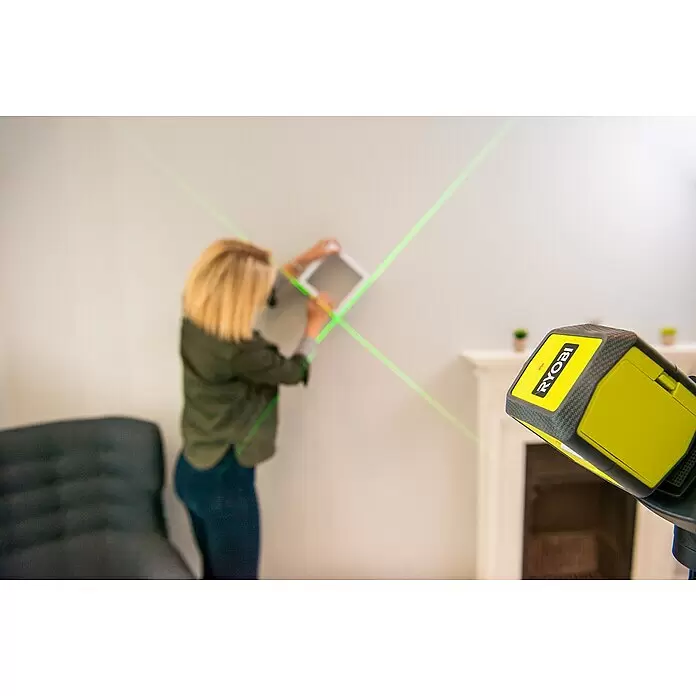 Ryobi Kreuzlinienlaser RBCLLG1 - Max. Arbeitsbereich: 15 m - Gelber und grauer Ryobi-Laser-Nivellierer projiziert grüne Linien an eine Wand, um eine Person beim Aufhängen eines Gegenstands zu unterstützen.