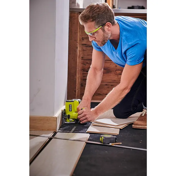 Ryobi ONE+ Akku-Tauchsäge R18MMS-0 - 18 V, Ohne Akku, Leerlaufdrehzahl: 4.250 U/min - Ein Mann arbeitet mit einem gelben Ryobi-Elektrowerkzeug an einer Holzarbeit in einem Innenraum, wobei er sorgfältig die Kante bearbeitet.