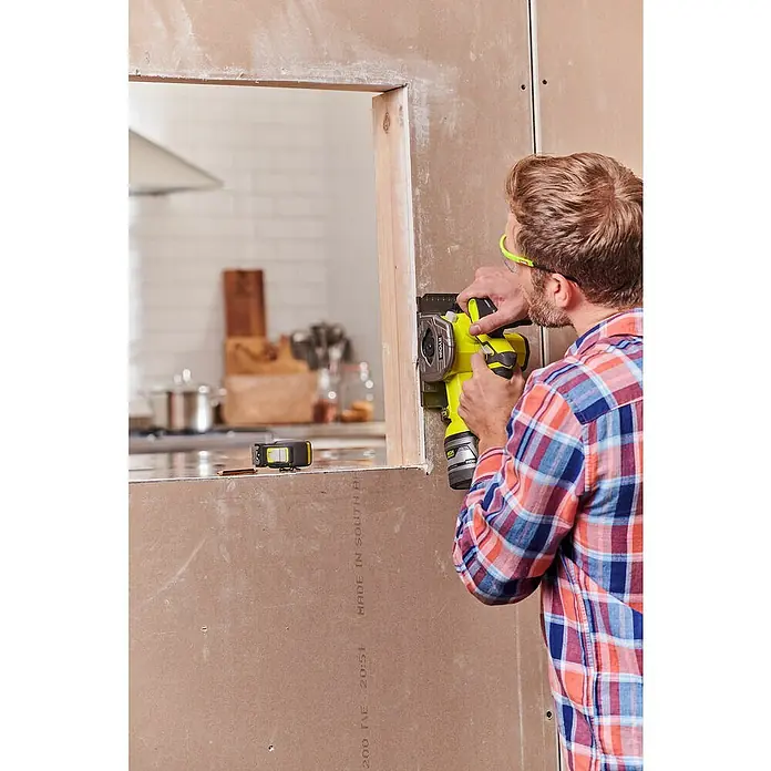 Ryobi ONE+ Akku-Tauchsäge R18MMS-0 - 18 V, Ohne Akku, Leerlaufdrehzahl: 4.250 U/min - Ein Mann benutzt ein gelbes Ryobi Elektrowerkzeug, um durch eine Gipskartonwand neben einer Holzöffnung zu schneiden.