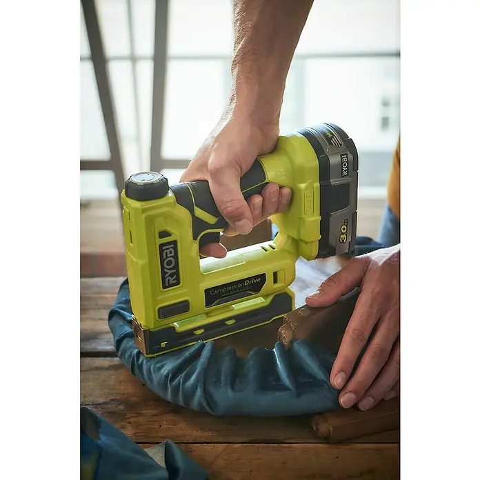 Ryobi ONE+ Akku-Tacker R18ST50-0 - 18 V, Li-Ionen, Anzahl Akkus: Ohne Akku - Nahaufnahme einer Person, die mit einem Ryobi-Tacker ein blaues Stoffstück an einem Holzrahmen befestigt.