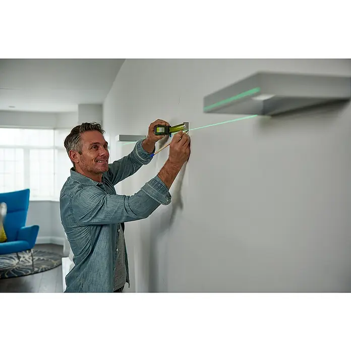 Ryobi Kreuzlinienlaser 360° RB360GLL - Max. Arbeitsbereich: 25 m - Mann befestigt mit Laserwasserwaage eine Wandhalterung. Präzises Nivellieren für die perfekte Montage von Regalen und mehr mit einem Laser.