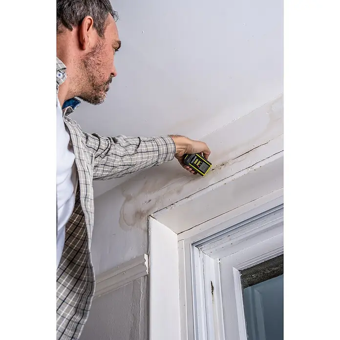 Ryobi Feuchtigkeitsmessgerät RBPINMM1 - Geeignet für: Baumaterialien/Holz - Ein Mann überprüft mit einem Ryobi Feuchtigkeitsmesser die Feuchtigkeit an einer Wand mit Rissen und Wasserflecken.