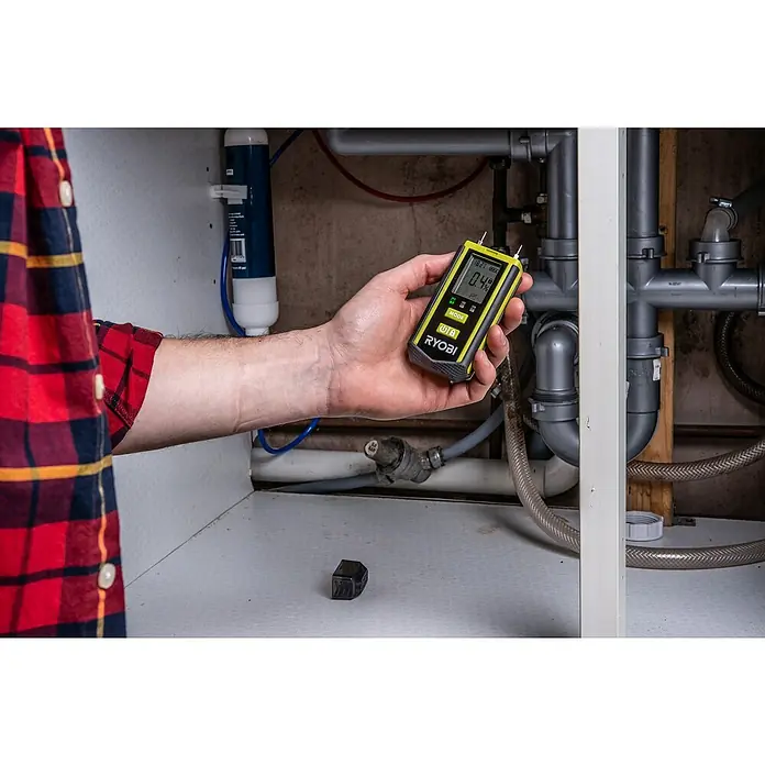 Ryobi Feuchtigkeitsmessgerät RBPINMM1 - Geeignet für: Baumaterialien/Holz - Hand, die ein RYOBI-Feuchtigkeitsmessgerät vor einem Waschbecken mit Rohrleitungen hält, um auf Lecks zu prüfen.