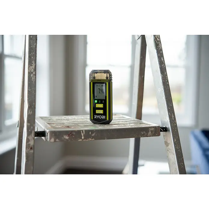 Ryobi Feuchtigkeitsmessgerät RBPINMM1 - Geeignet für: Baumaterialien/Holz - Ryobi Feuchtigkeitsmessgerät auf einer Leiterstufe, das den Feuchtigkeitsgehalt mit 7,4 % anzeigt, nützlich für Bau- und Renovierungsarbeiten.
