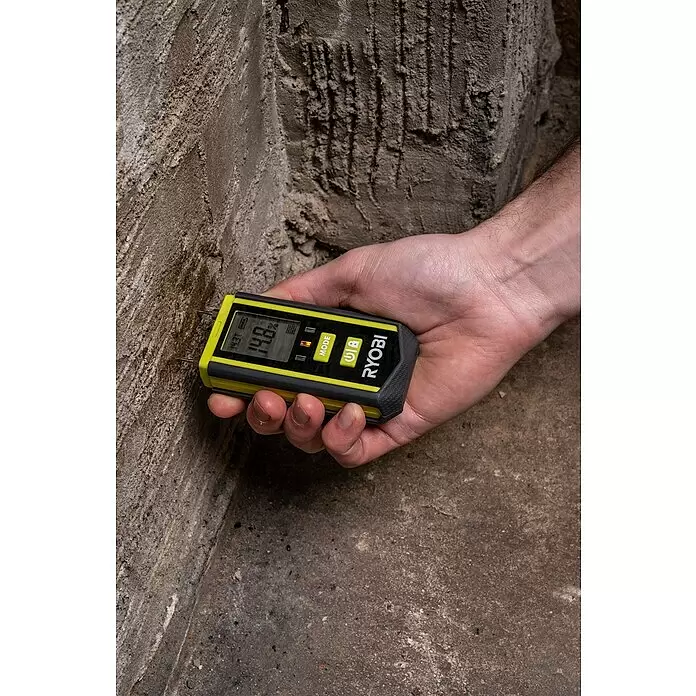 Ryobi Feuchtigkeitsmessgerät RBPINMM1 - Geeignet für: Baumaterialien/Holz - Hand hält gelbes und schwarzes Ryobi Feuchtigkeitsmessgerät an Betonwand, zeigt 14,8% Feuchtigkeit.