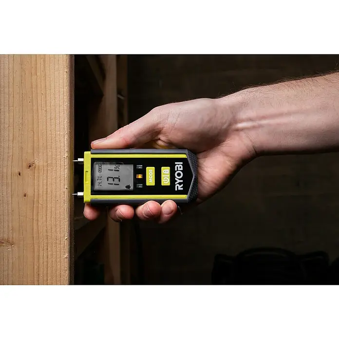 Ryobi Feuchtigkeitsmessgerät RBPINMM1 - Geeignet für: Baumaterialien/Holz - Nahaufnahme eines RYOBI Feuchtigkeitsmessgeräts, das an einem Holzbrett befestigt ist und den Feuchtigkeitsgehalt anzeigt.