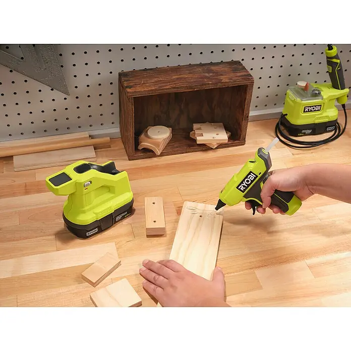 Ryobi ONE+ Akku-Heißklebepistole RGLM18-018 V, Ohne Akku, Durchmesser Klebepatrone: 7 mm - Nahaufnahme einer Person, die ein RYOBI-Werkzeug zum Verkleben von Holz verwendet, auf einer Werkbank mit anderem Werkzeug.