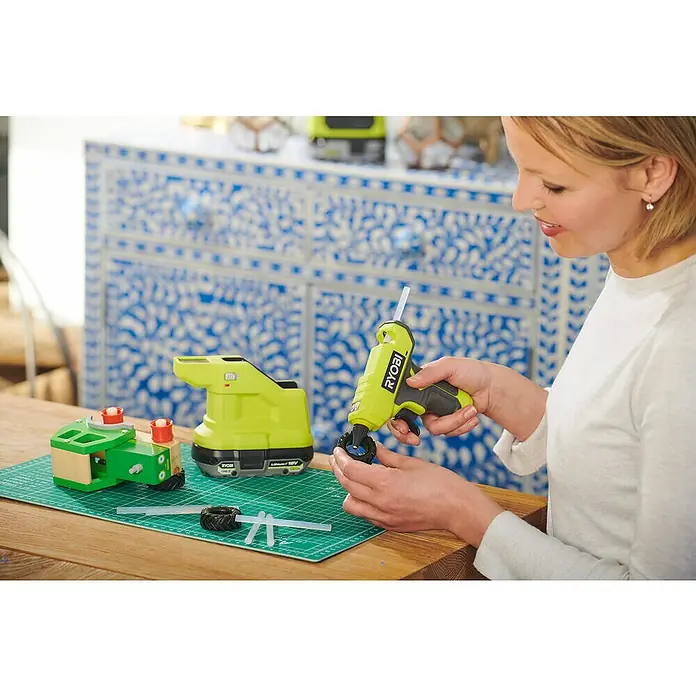 Ryobi ONE+ Akku-Heißklebepistole RGLM18-0 - 18 V, Ohne Akku, Durchmesser Klebepatrone: 7 mm - Bastelprojekt mit RYOBI Klebepistole: Eine Frau klebt ein Rad an ein Holzspielzeug. Die Akku-Heißklebepistole ermöglicht kabelloses Arbeiten.