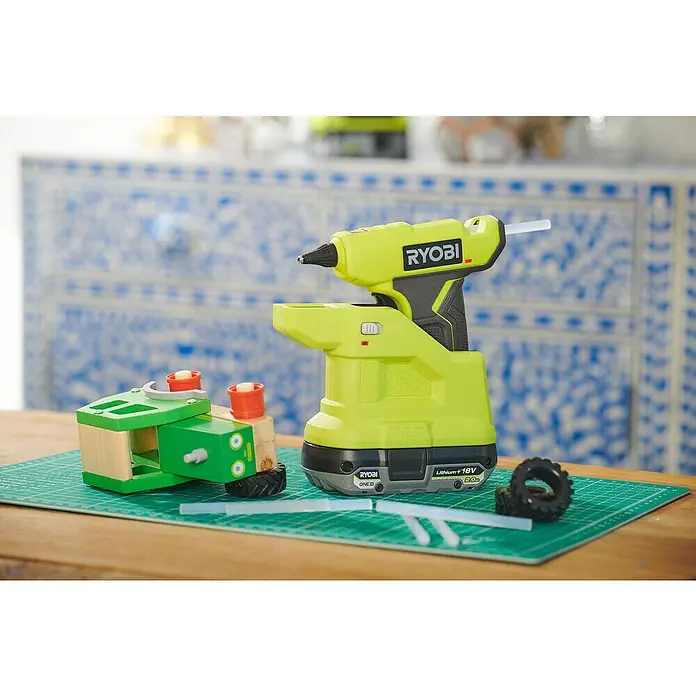 Ryobi ONE+ Akku-Heißklebepistole RGLM18-0 - 18 V, Ohne Akku, Durchmesser Klebepatrone: 7 mm - Ryobi Klebepistole mit Akku und ein selbstgebautes Holzspielzeug auf einer Schneidematte.