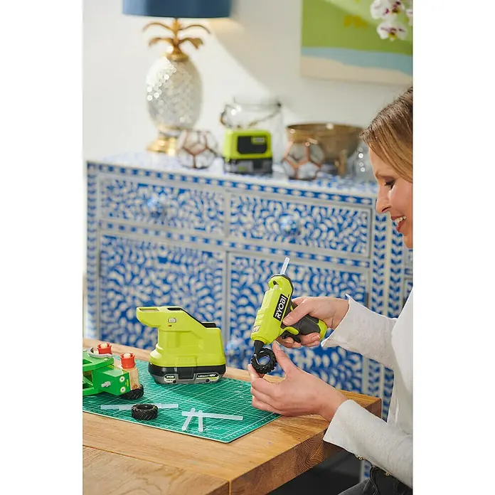 Ryobi ONE+ Akku-Heißklebepistole RGLM18-018 V, Ohne Akku, Durchmesser Klebepatrone: 7 mm - Nahaufnahme einer Frau, die mit einer RYOBI Akku-Klebepistole und verschiedenen Werkzeugen an einem Bastelprojekt arbeitet.