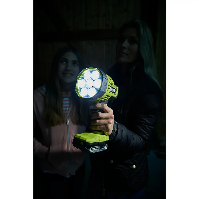 Ryobi ONE+ LED Baustrahler RLS18-0 - 3.000 lm, 3-Stufen-LED - Eine Frau hält eine Ryobi 3000 Lumen ONE+ Akku-Arbeitsleuchte, die eine andere Person beleuchtet, für den Einsatz im Dunkeln.