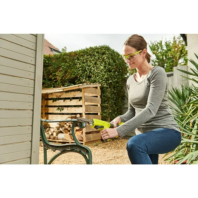Ryobi ONE+ Maschinenpaket - Akku-Bandschleifer R18PF-0 + gratis Starter-Kit - Frau schleift eine grüne Bank mit einem Bandschleifer im Garten, Schutzbrille inklusive.