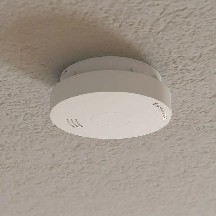 Rauchwarnmelder VdS - Durchmesser: 10 cm, Batterielaufzeit: 10 Jahre, Alarmsignal: 85 dB - Ein weißer Rauchmelder ist an einer strukturierten Decke montiert und sorgt für Sicherheit im Haus.