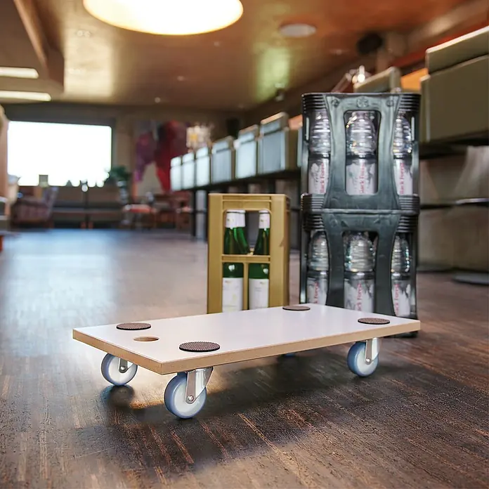 Wagner System Transportroller MM 1318 - L x B x H: 575 x 300 x 100 mm, Traglast: 200 kg, Holz - Eine weiße Rollplatte mit Lenkrollen und Antirutschmatten, ideal für den Transport von Getränkekisten in Gastronomiebetrieben.