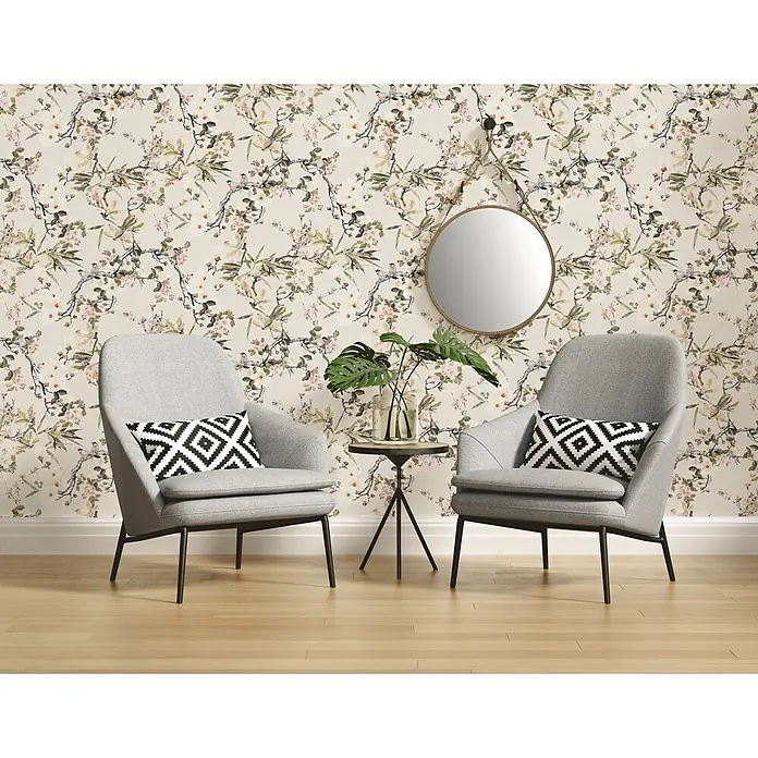 A.S. Création Michalsky Vliestapete Zweige - Bunt, Floral, 10,05 x 0,53 m - Zwei graue Sessel mit geometrischen Kissen vor einer floralen Tapete. Ein runder Spiegel hängt an der Wand über einem kleinen Tisch mit einer Pflanze.