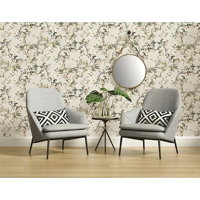 A.S. Création Michalsky Vliestapete Zweige - Bunt, Floral, 10,05 x 0,53 m - Zwei graue Sessel mit geometrischen Kissen vor einer floralen Tapete. Ein runder Spiegel hängt an der Wand über einem kleinen Tisch mit einer Pflanze.