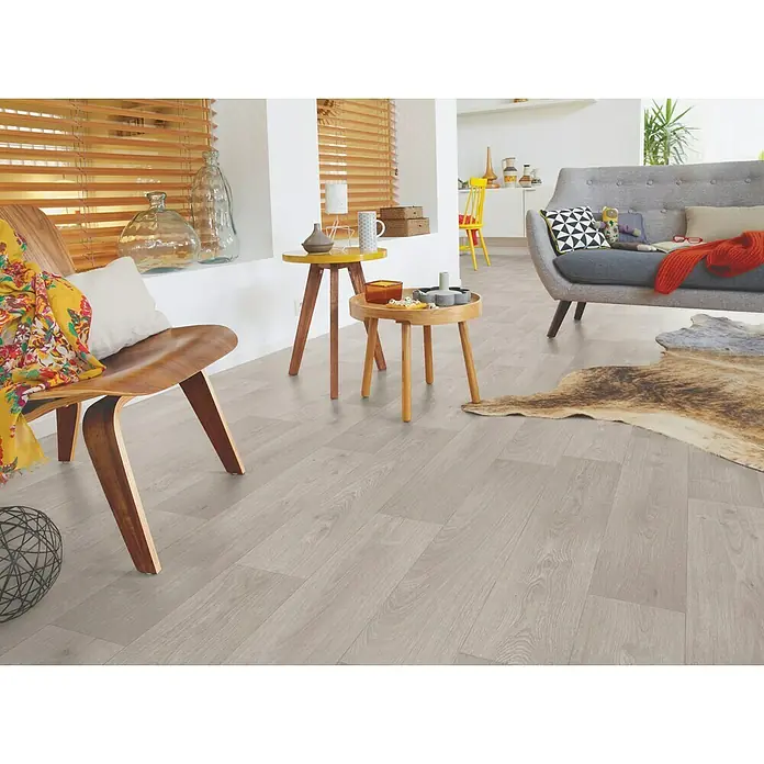 Tarkett Suelo de PVC a metros Woodstyle - Efecto madera, Ancho: 4 m - Interior luminoso con un sofá moderno, una mesa de centro y una silla sobre un suelo de madera gris.