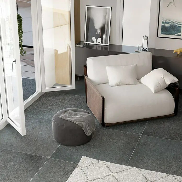 Feinsteinzeugfliese Erawan Negro - 100 x 100 cm, Grau, Matt - Ein gemütlicher Sessel mit Ottomane lädt zum Entspannen ein. Die Farbtöne sind neutral gehalten, was für eine ruhige Atmosphäre sorgt.