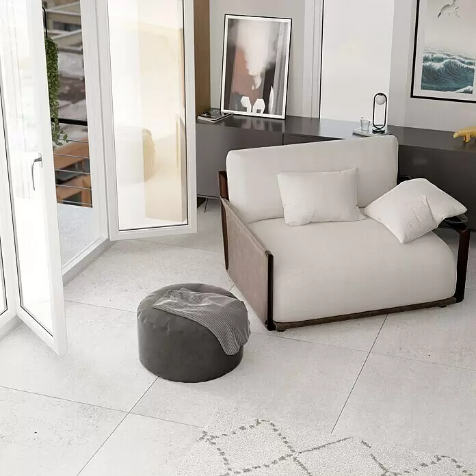 Feinsteinzeugfliese Homestone Grey - 100 x 100 cm, Grau, Matt - Modernes Wohnzimmer mit hellem Sessel mit dunklen Holzakzenten und einem dunkelgrauen Stoffhocker mit Decke, neben einer offenen Balkontür.
