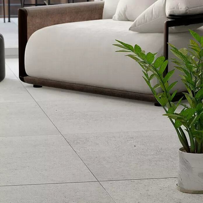 Feinsteinzeugfliese Homestone Grey - 100 x 100 cm, Grau, Matt - Hellgraue, strukturierte Bodenfliesen in einem modernen Wohnraum mit Sofa und Topfpflanze.