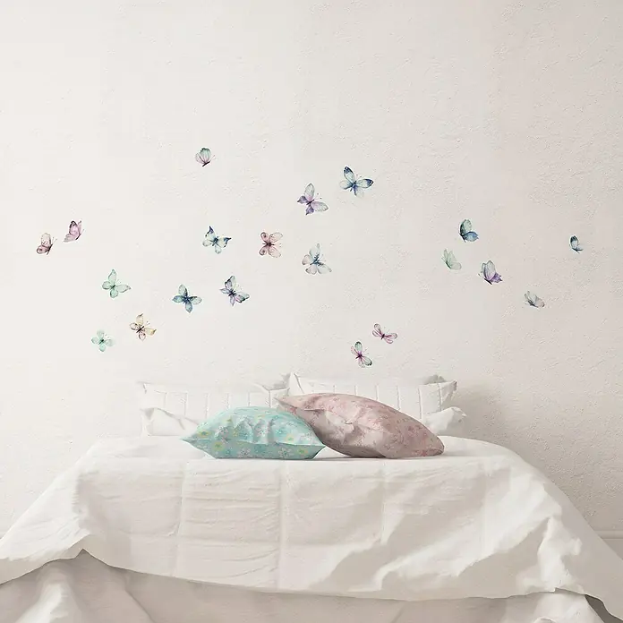 Vinilo de pared Mariposas acuarela - Multicolor, Plástico - Decoración de pared con delicados motivos de mariposas sobre una cama acogedora con almohadas, ideal para un ambiente tranquilo en el dormitorio.