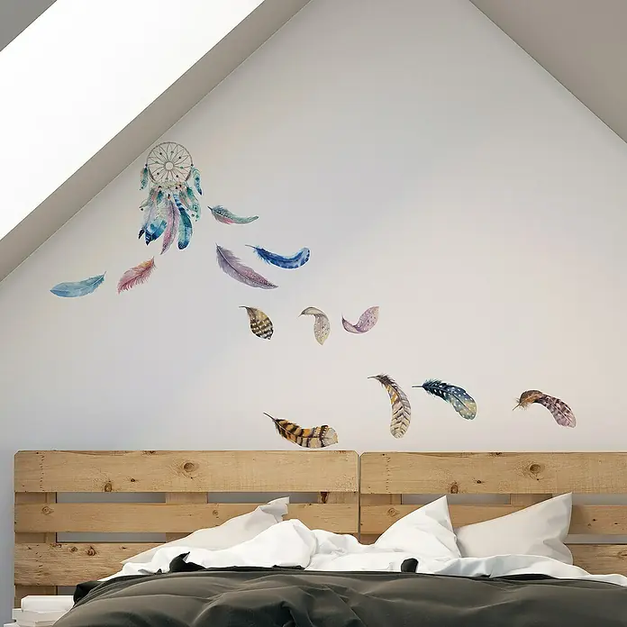 Vinilo de pared Atrapasueño acuarela - Multicolor, Plástico - Decoración de pared con atrapasueños y plumas sobre una cama de madera con ropa de cama blanca y una colcha gris para un ambiente tranquilo.