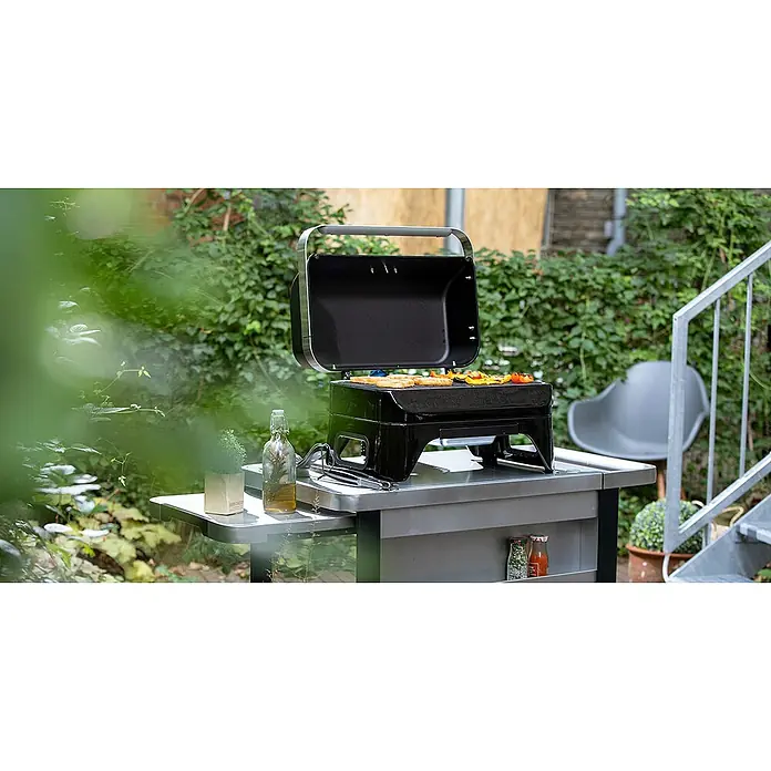 Campingaz Barbacoa de gas Attitude 2GO - Número de quemadores: 1 - Parrilla con tapa abierta y comida en la parrilla. La parrilla está colocada sobre una mesa en el jardín y lista para usar.