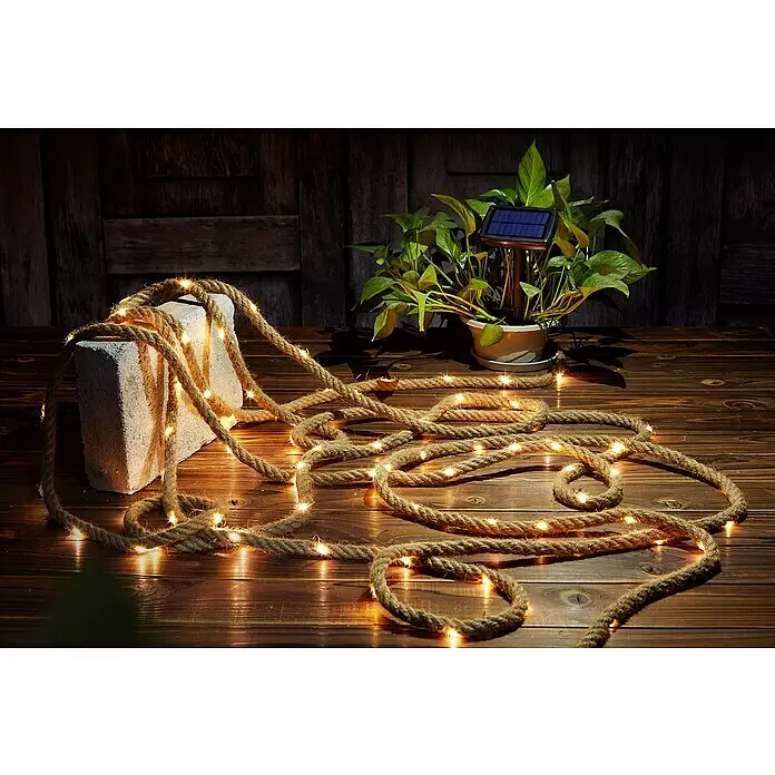 BAUHAUS Solar-Lichterkette - Länge: 13 m, LED - Beleuchtete Jute-Seilleuchte mit warmen Lichtern, dekorativ auf rustikaler Holzoberfläche drapiert.