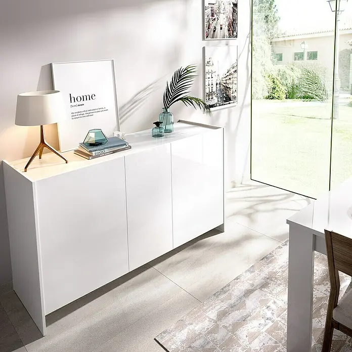 Dekit Aparador Kloe - L x An x Al: 42 x 138 x 76 cm, Blanco/Natural, Número de puertas: 3 ud. - Un aparador blanco brillante con un diseño minimalista, decorado con una lámpara y jarrones, se encuentra contra una pared con cuadros.