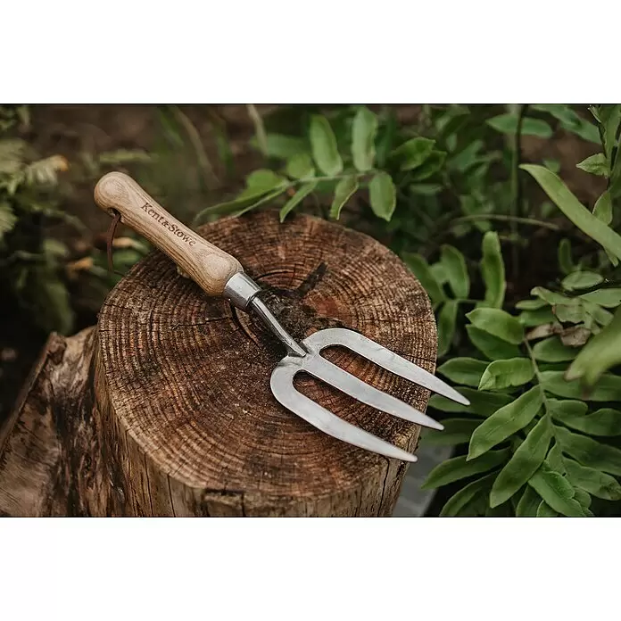 Kent & Stowe Handgabel - 5 cm, 3 - Eine kleine Gartenkralle mit Holzgriff, graviert mit 'Kent & Stowe', und silbernen Zinken, ruhend auf einem Holzstamm.