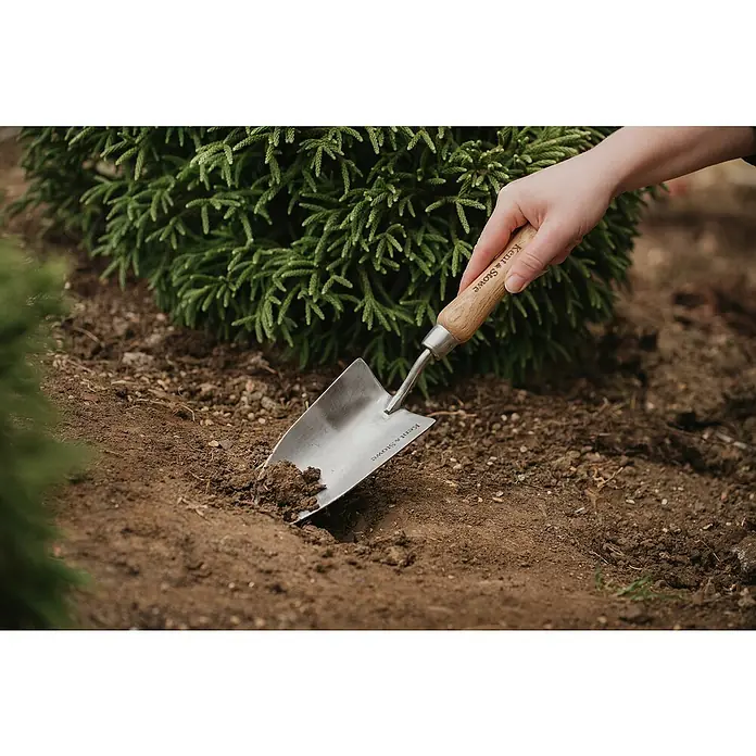 Kent & Stowe Blumenkelle - 8,5 cm - Nahaufnahme eines Kent & Stowe Gartenwerkzeugs, das in die Erde gesteckt wird, mit einer Hand am Holzgriff, ideal für Gartenarbeiten.
