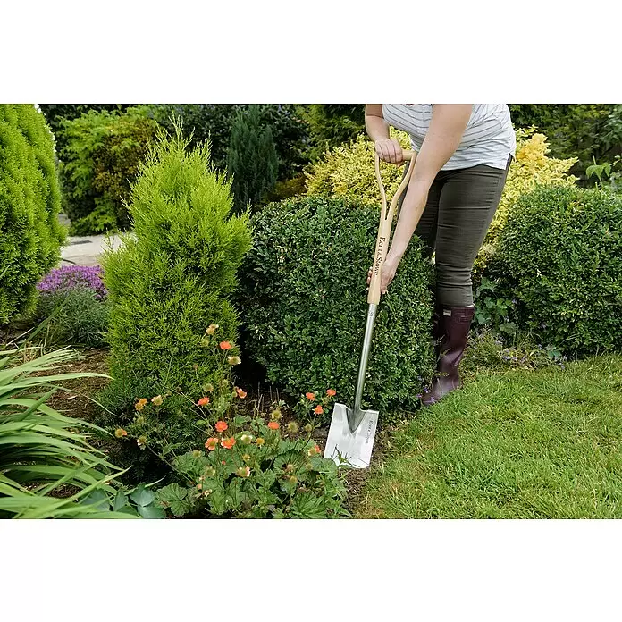 Kent & Stowe Gärtnerspaten - Arbeitsbreite: 14 cm, Langstiel - Person gräbt mit einem Kent & Stowe Spaten mit Holzgriff und silberner Schaufel im Garten.