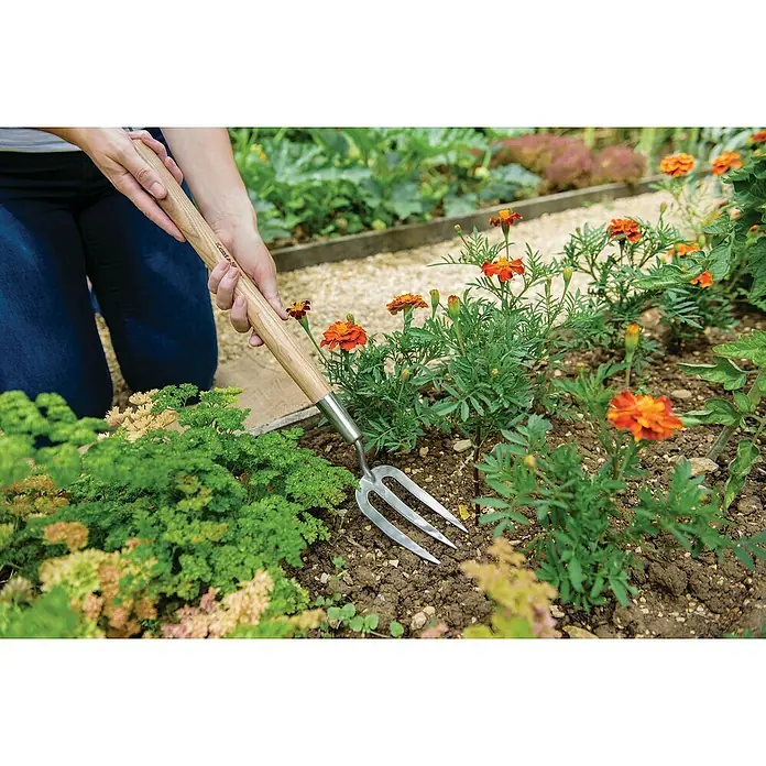 Kent & Stowe HandgabelMaße Blatt: 215 x 105 mm, Anzahl Zinken: 3 - Nahaufnahme einer Person, die im Garten arbeitet, mit einer Kent & Stowe Garten Gabel, um Pflanzen zu pflegen.