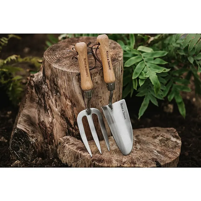 Kent & Stowe Blumenkelle - 8,5 cm - Nahaufnahme eines Kent & Stowe Gartengabel und einer Schaufel, die auf einem Baumstumpf platziert sind. Ideal für Gartenliebhaber!