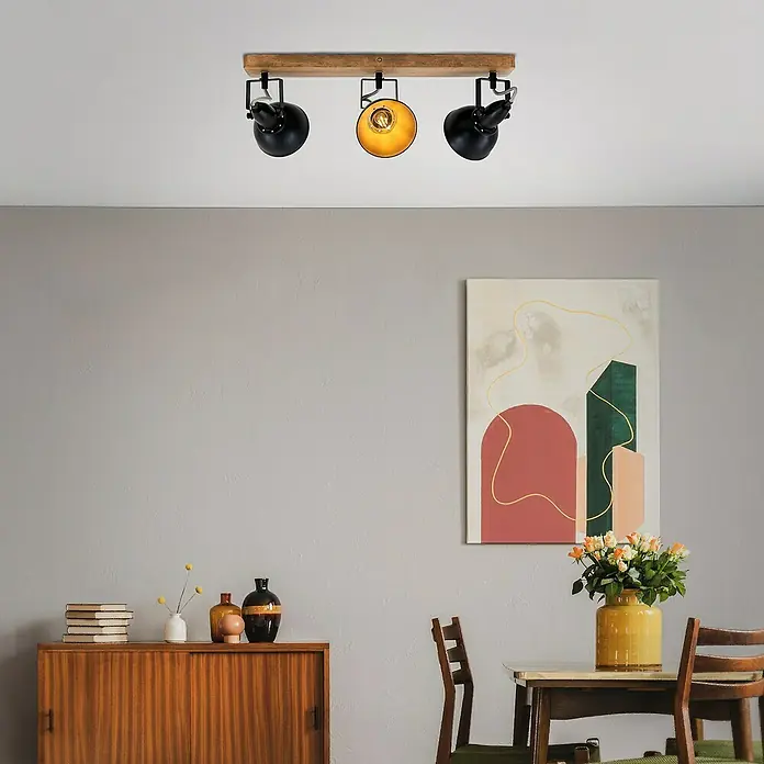 Briloner Barnim Regleta - 75 W, L x An x Al: 50 x 11 x 15,7 cm, Negro/Marrón, Negro/Dorado, E14, 3 ud. - Lámpara de techo con tres focos negros sobre una barra de madera. Un foco está encendido, iluminando la habitación con luz cálida.