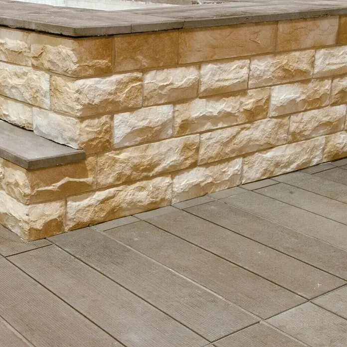 Revestimiento de piedra Cantabria - Pardo, Cantidad total: 4 pzs. - Primer plano de una pared de piedra de color arena sobre una plataforma de madera, mostrando la textura y la paleta de colores de ambos materiales.