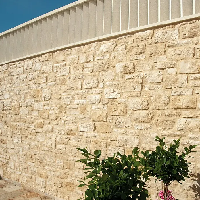 Revestimiento de piedra Silleria Cobre - Cobre, Cantidad total: 4 pzs. - Primer plano de una pared de piedra beige con un árbol decorativo, destacando su textura y mampostería.
