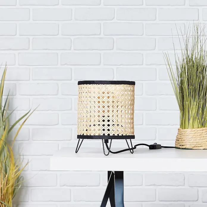 Brilliant Wiley Tischleuchte - 60 W, Schwarz, E27 - Tischlampe mit einem Lampenschirm aus Rattan und einem schwarzen Metallfuß auf einem weißen Tisch.