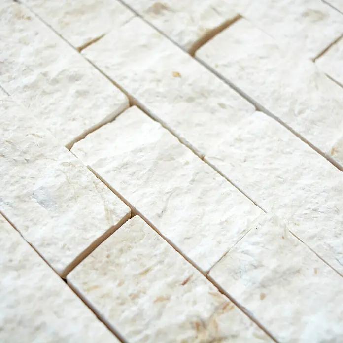 Mosaikfliese Brick Splitface X3D 49248 - 30,5 x 29 cm, Weiß, Matt - Nahaufnahme einer dekorativen Wandverkleidung aus hellen, rechteckigen Steinen mit natürlicher Textur und subtilen Farbunterschieden.