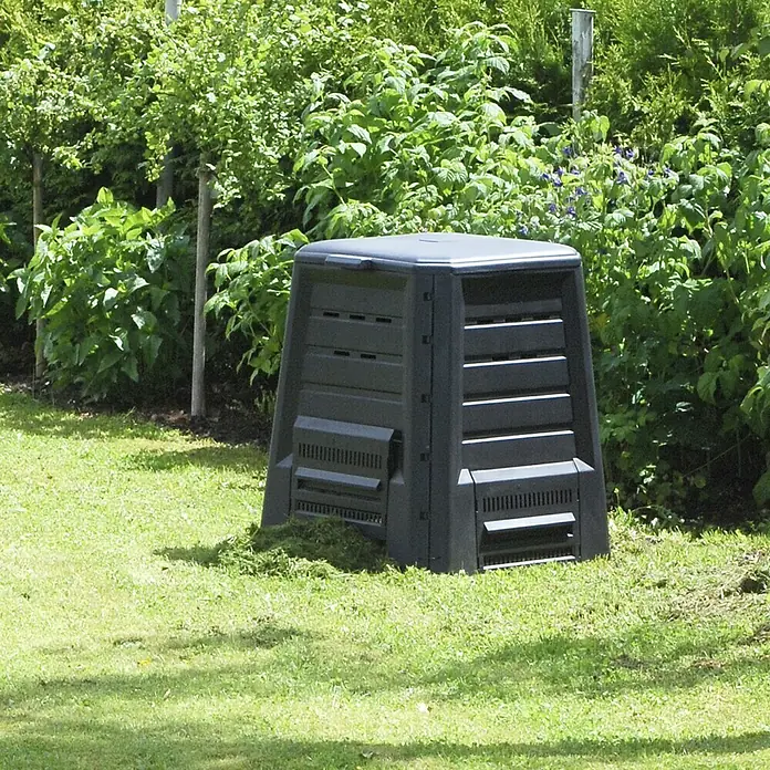 KHW Komposter - 340 l, 75 x 75 x 87 cm - Eine schwarze Kompostkiste steht auf einem grünen Rasen vor einem grünen Busch im Garten. Sieht aus, als würde sie zum Kompostieren benutzt.