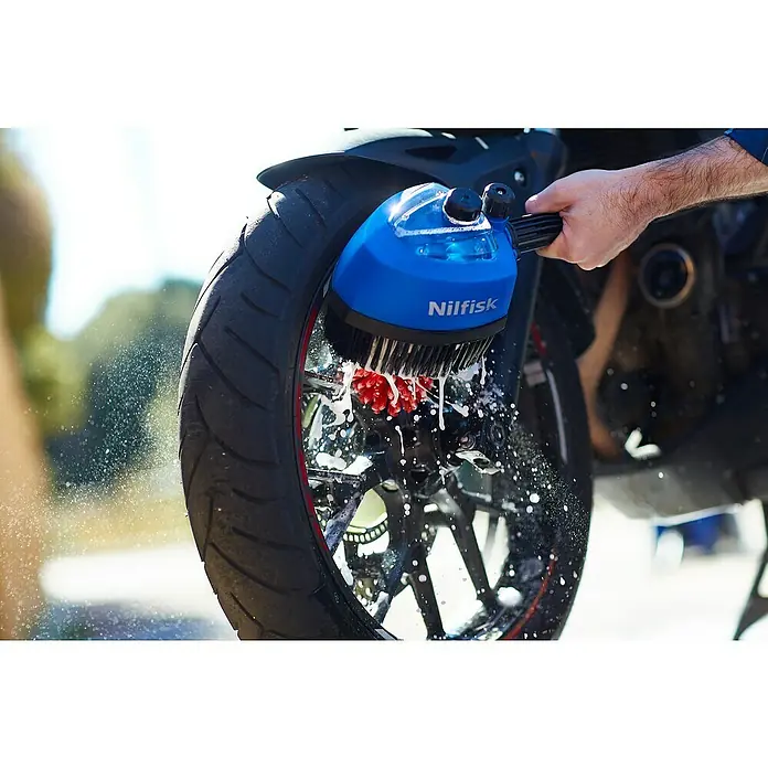 Nilfisk Cepillo para automóviles giratorio - Específico para: Limpiadoras de alta presión Nilfisk - Se utiliza un accesorio de cepillo Nilfisk para limpiar la rueda de una motocicleta, rociando agua y jabón mientras el cepillo friega la rueda.