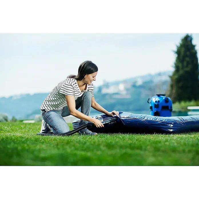 Nilfisk Elektro-Nass- & Trockensauger Multi II 30 T EU - 1.400 W, Behältervolumen: 30 l, Halbautomatisch - Frau pumpt mit einer elektrischen Pumpe eine aufblasbare blaue Matratze auf einer grünen Wiese auf.