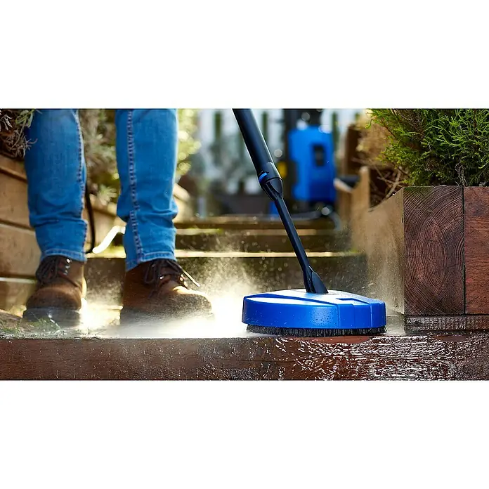Nilfisk Accesorio de limpieza para suelos exteriores Compact Patio - Específico para: Limpiadoras de alta presión Nilfisk - Una persona usa un limpiador de superficies azul conectado a una hidrolavadora para limpiar una plataforma de madera.