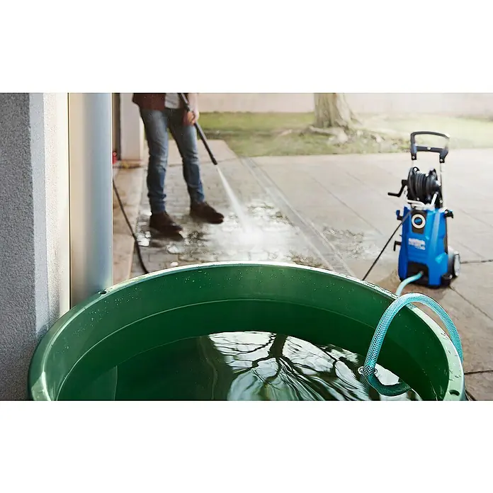 Nilfisk Manguera de aspiración - Largo: 3 m - Una hidrolimpiadora está funcionando desde una tina de agua verde con una manguera azul mientras una persona limpia un patio.