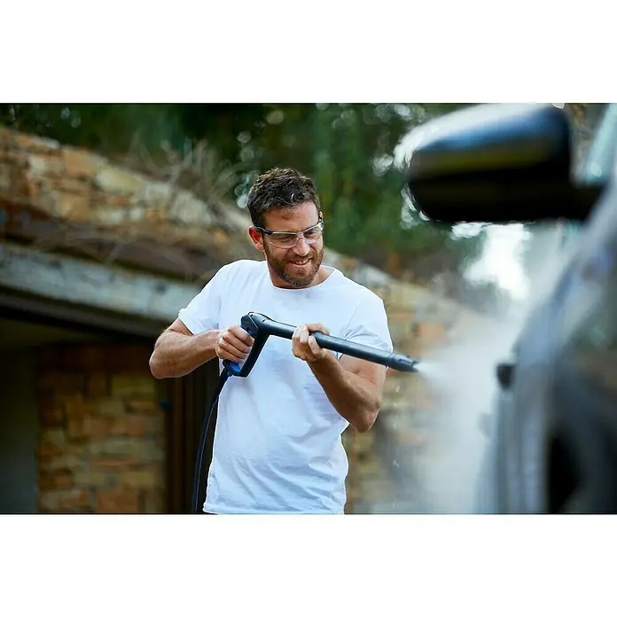 Nilfisk Hidrolimpiadora de alta presión E160.1-10 H X-TRA EU - 160 bar, 2.300 W, Capacidad de bombeo: 500 l/h - Hombre lavando un coche con una hidrolavadora al aire libre, usando gafas de seguridad y camiseta blanca, enfoque en el equipo de limpieza.