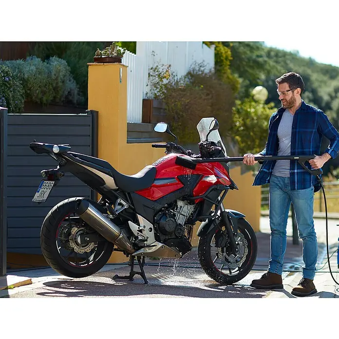 Nilfisk Hidrolimpiadora de alta presión CORE 140IH PCH - 140 bar, 1.800 W, Capacidad de bombeo: 474 l/h - Hombre limpiando una motocicleta roja con una hidrolavadora al aire libre, mostrando el equipo y el proceso de limpieza.