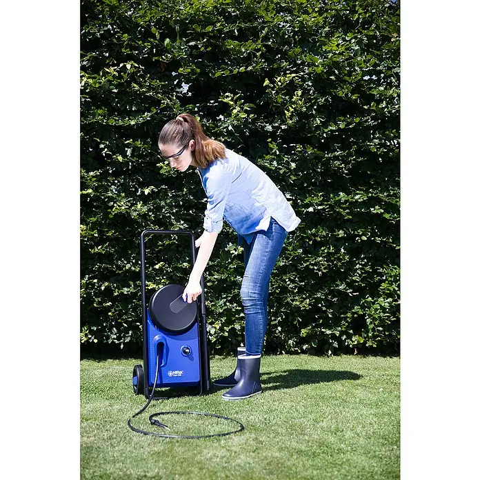 Nilfisk Hidrolimpiadora de alta presión CORE 140IH PCH - 140 bar, 1.800 W, Capacidad de bombeo: 474 l/h - Mujer operando una hidrolimpiadora Nilfisk azul, con un cable eléctrico tirado en el césped.
